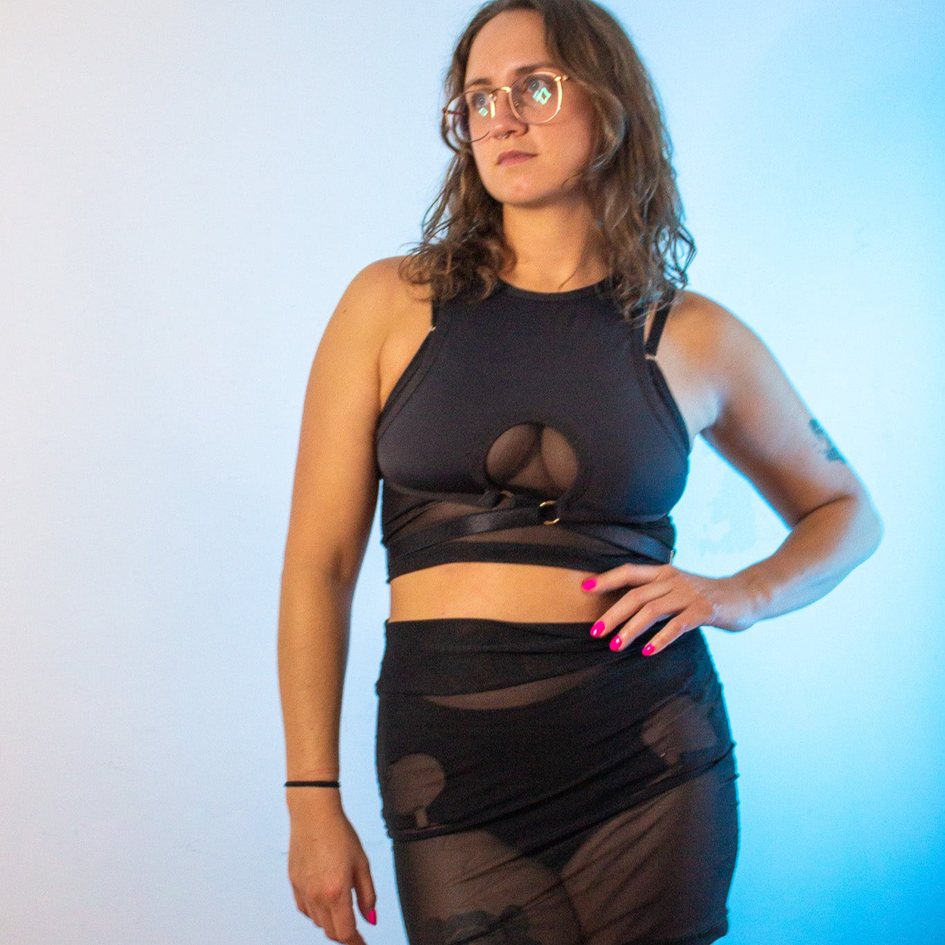 Woman wearing a black outfit with sheer elements against a gradient background